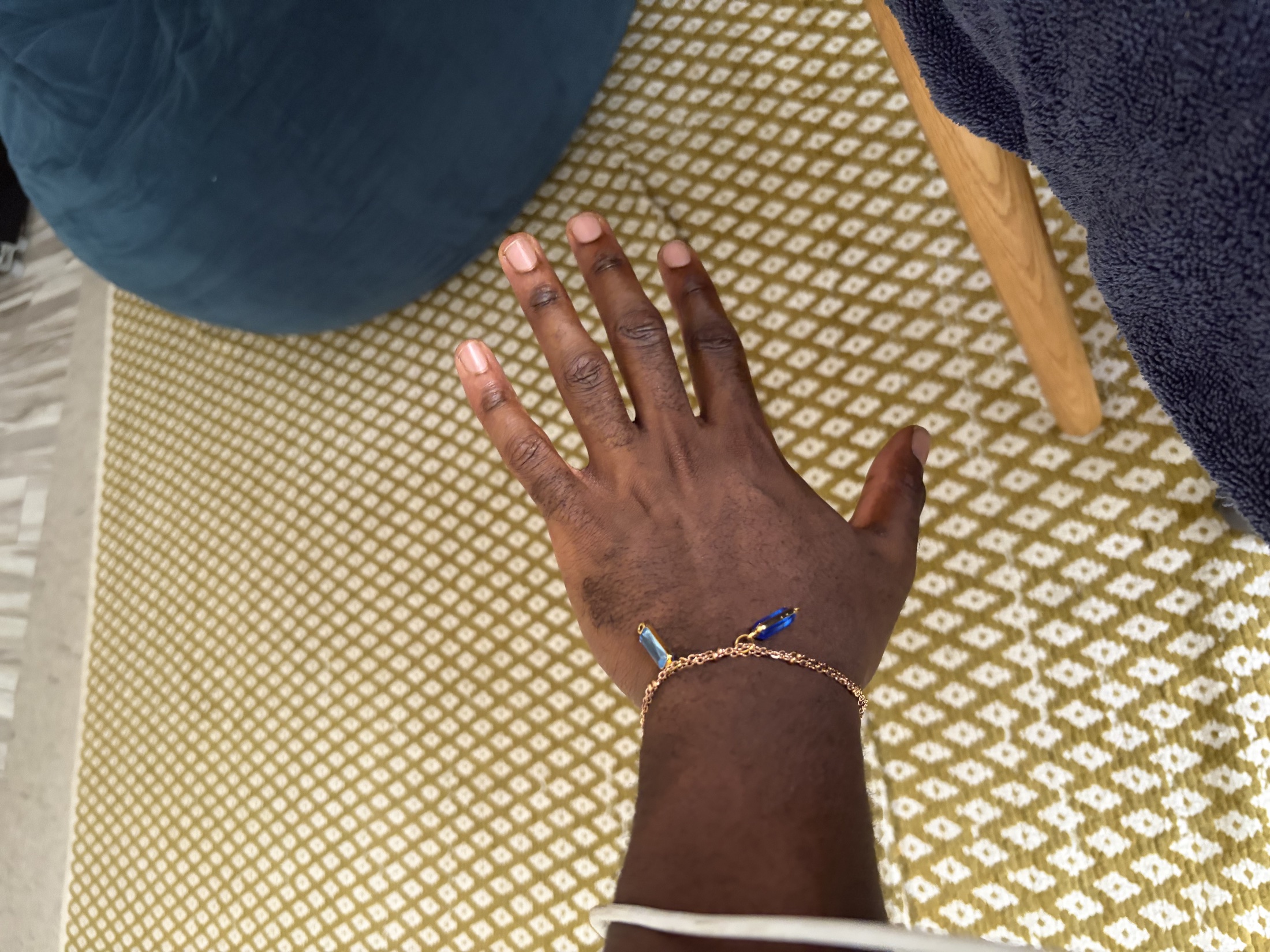 A wrist wearing a fine gold bracelet with vivid blue baguette charms.