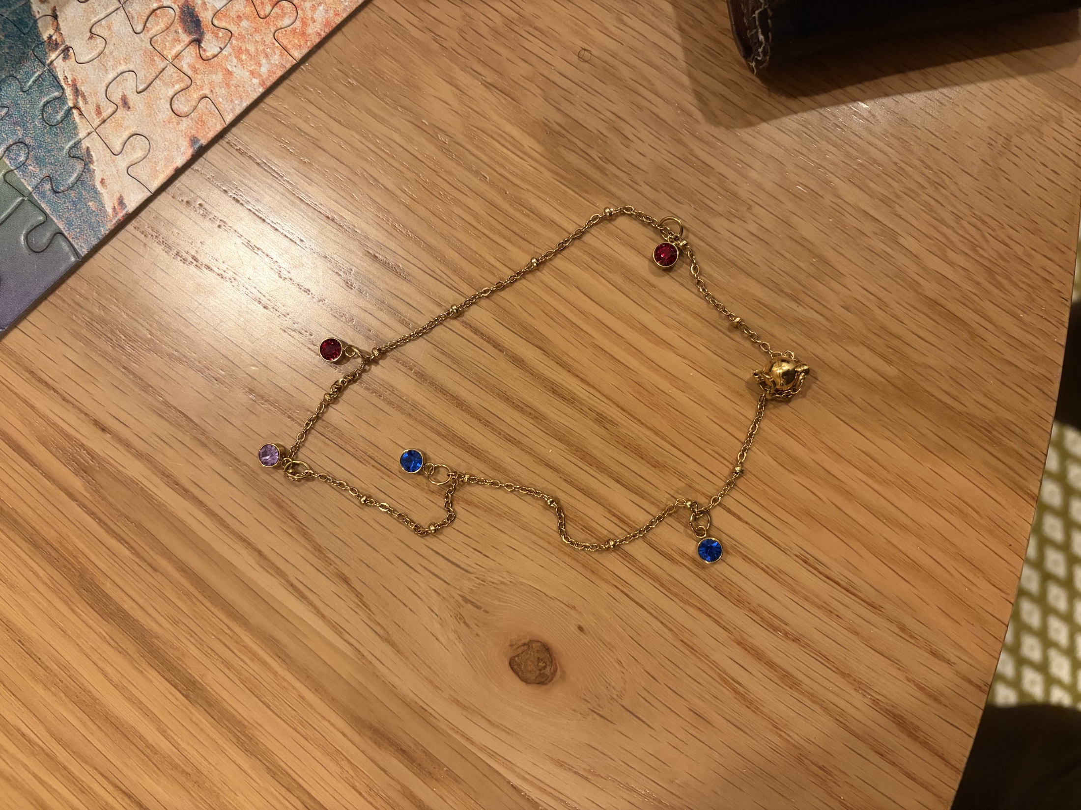 A fine gold bracelet with blue, red, and violet charms arranged on soft fabric.